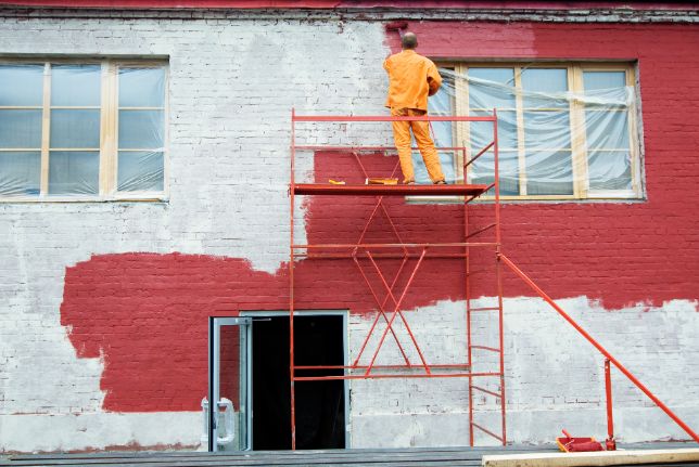 House construction worker painting the building standing on a ladder